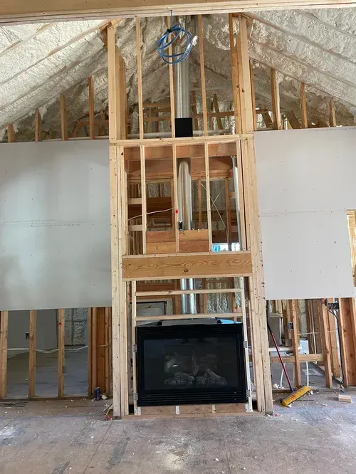 Unfinished home interior with exposed framing, a central fireplace, and insulation under the roof.