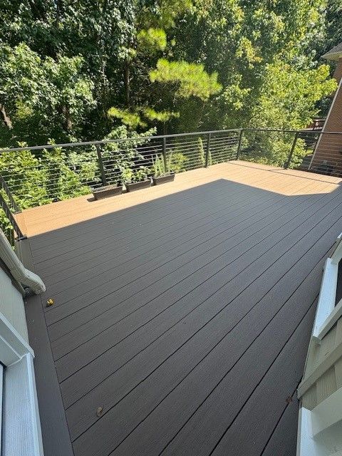 A modern two-tone deck with dark brown planks and a lighter brown border, featuring a cable railing overlooking trees.