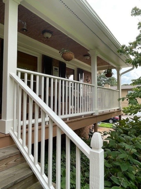 A white wooden staircase and porch railing attached to the front of a house with a covered wooden porch.