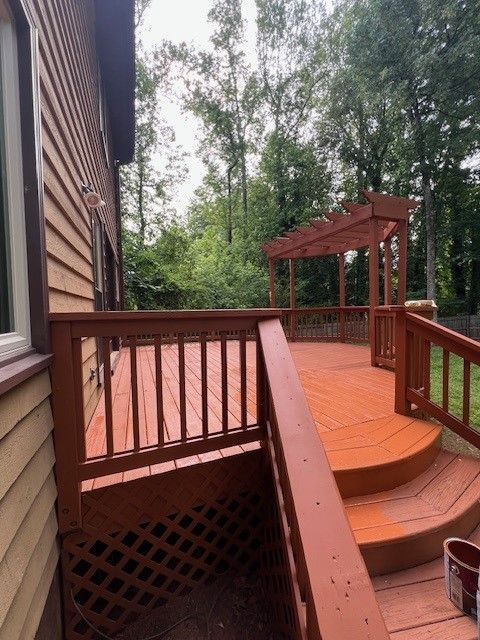 A freshly stained reddish-brown wooden deck with a matching pergola and stairs leading down into a lush green backyard.