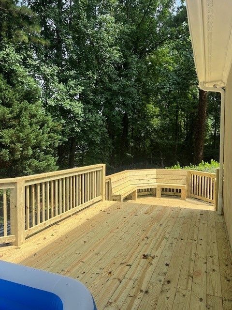 A newly constructed light-wood deck with built-in bench seating, overlooking a dense forest area.