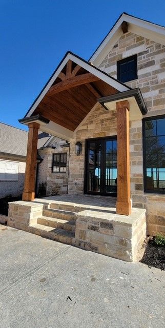 Stone house front porch with wood posts, peaked roof, and black double doors