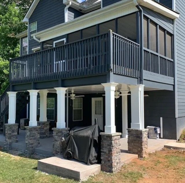 Two-story gray house with a large screened porch, white columns, and stone porch supports