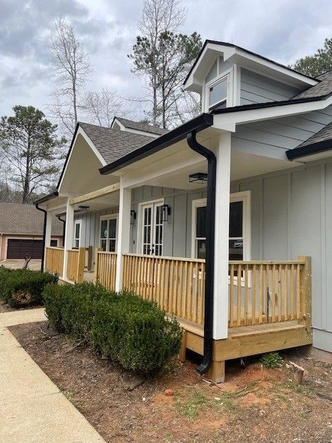Front view of a white house with a small wooden porch and black downspout along a curved walkway.