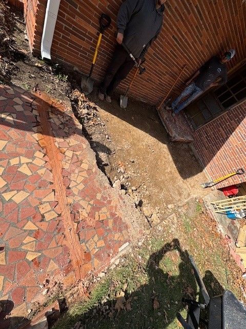 Tilted view of a backyard patio with brick walls, a mosaic stone floor, and a grassy area with shadows