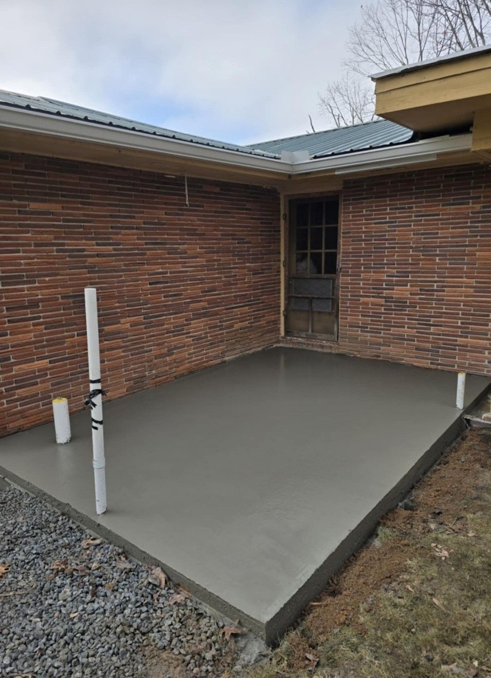 New concrete patio slab beside a brick house wall and roof eaves