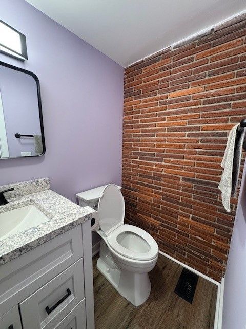 Small bathroom with white vanity, toilet, lavender wall, and brick accent wall