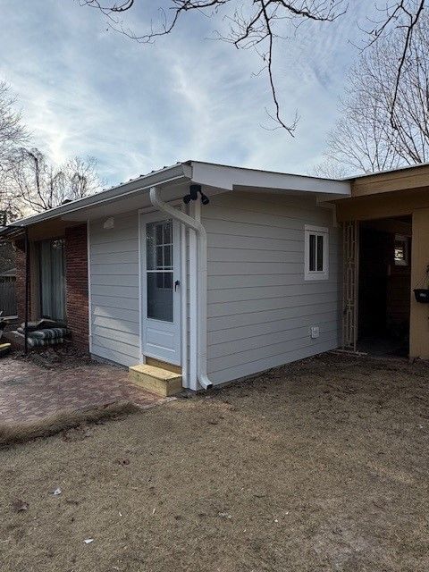Small gray house with a covered carport and screened front door, viewed from the yard.