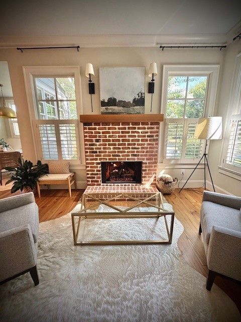 Bright living room with brick fireplace, large windows, neutral furniture, and a glass coffee table