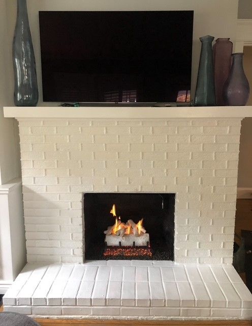 White brick fireplace with a small fire, topped by a TV and decorative vases