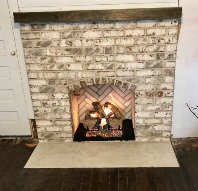 White brick fireplace with a lit fire, dark wood mantel, and pale hearth in a living room