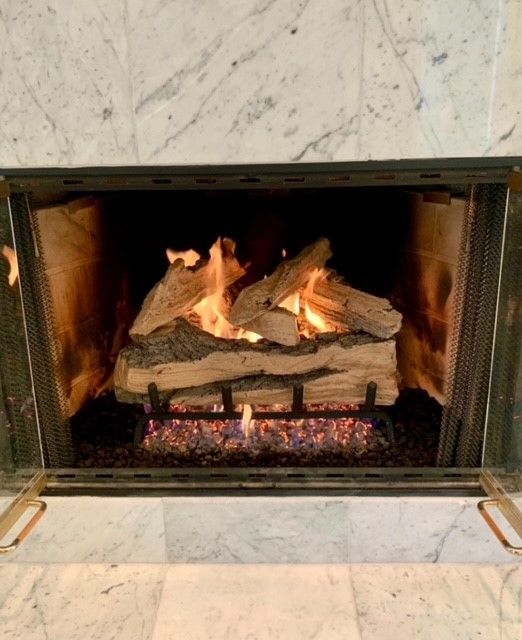 Lit fireplace with burning logs inside a marble surround