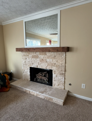 Living room fireplace with stone surround, wooden mantel, and mirror on a beige wall