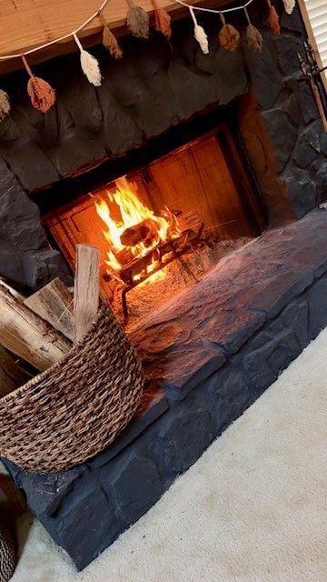 Cozy fireplace with burning logs, stone surround, and a wicker basket nearby