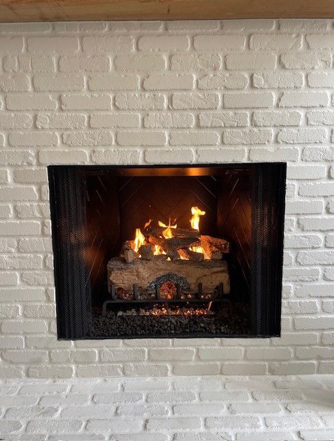Lit fireplace with flames in a white painted brick wall.