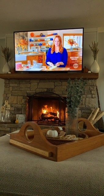 Living room with a lit stone fireplace, TV above the mantel, and a wooden tray on the carpeted floor