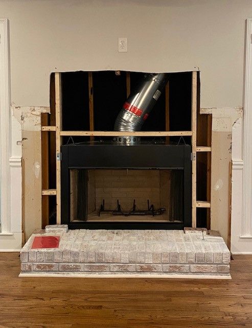 Partially demolished fireplace with exposed ducting, black firebox, and unfinished wall framing in a room