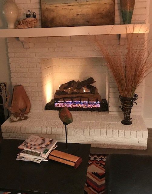 Cozy living room fireplace with glowing fire, brick surround, and decorative vases and books on a table