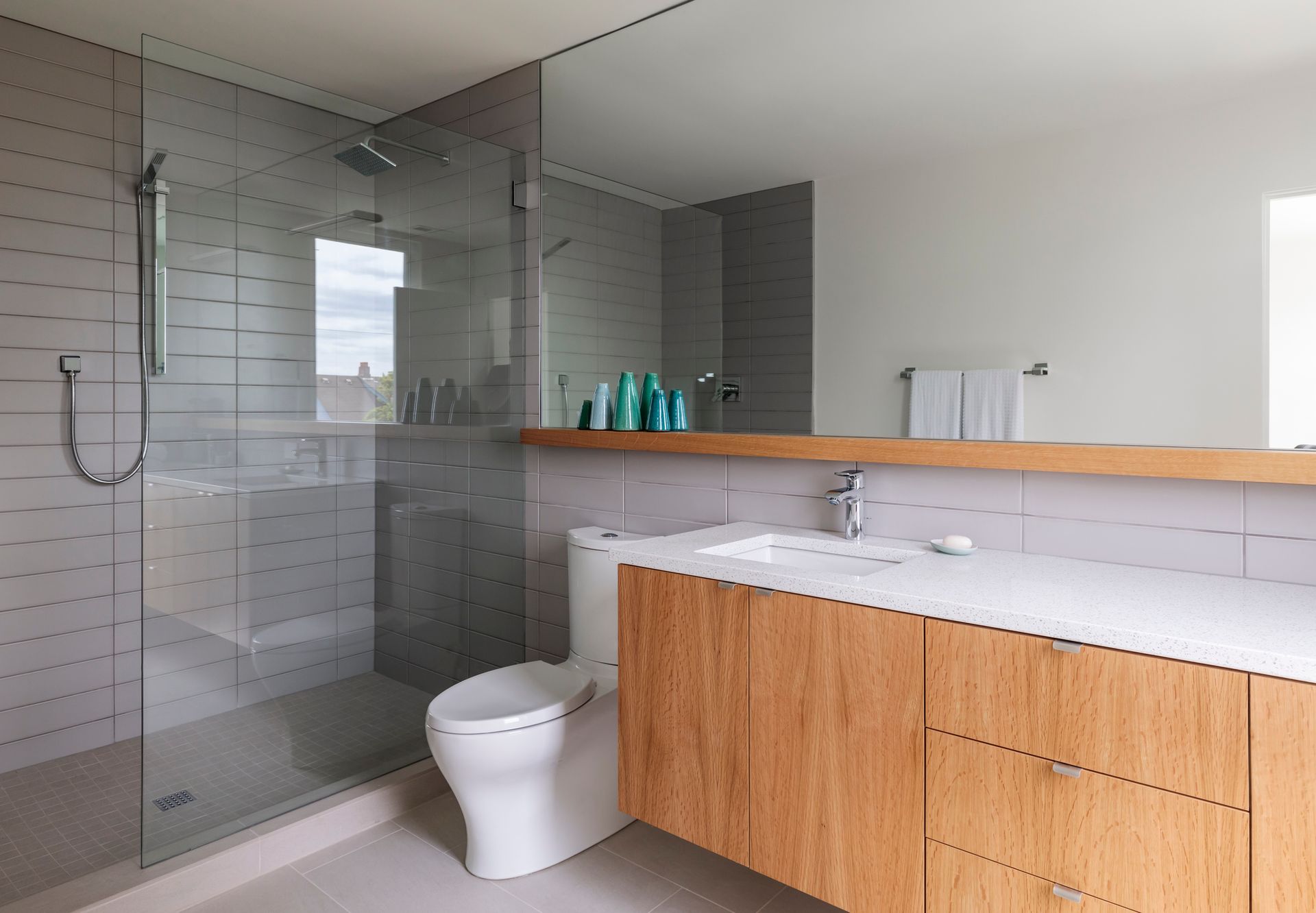 Modern bathroom with glass shower, wood vanity, white toilet, and mirror reflecting natural light.