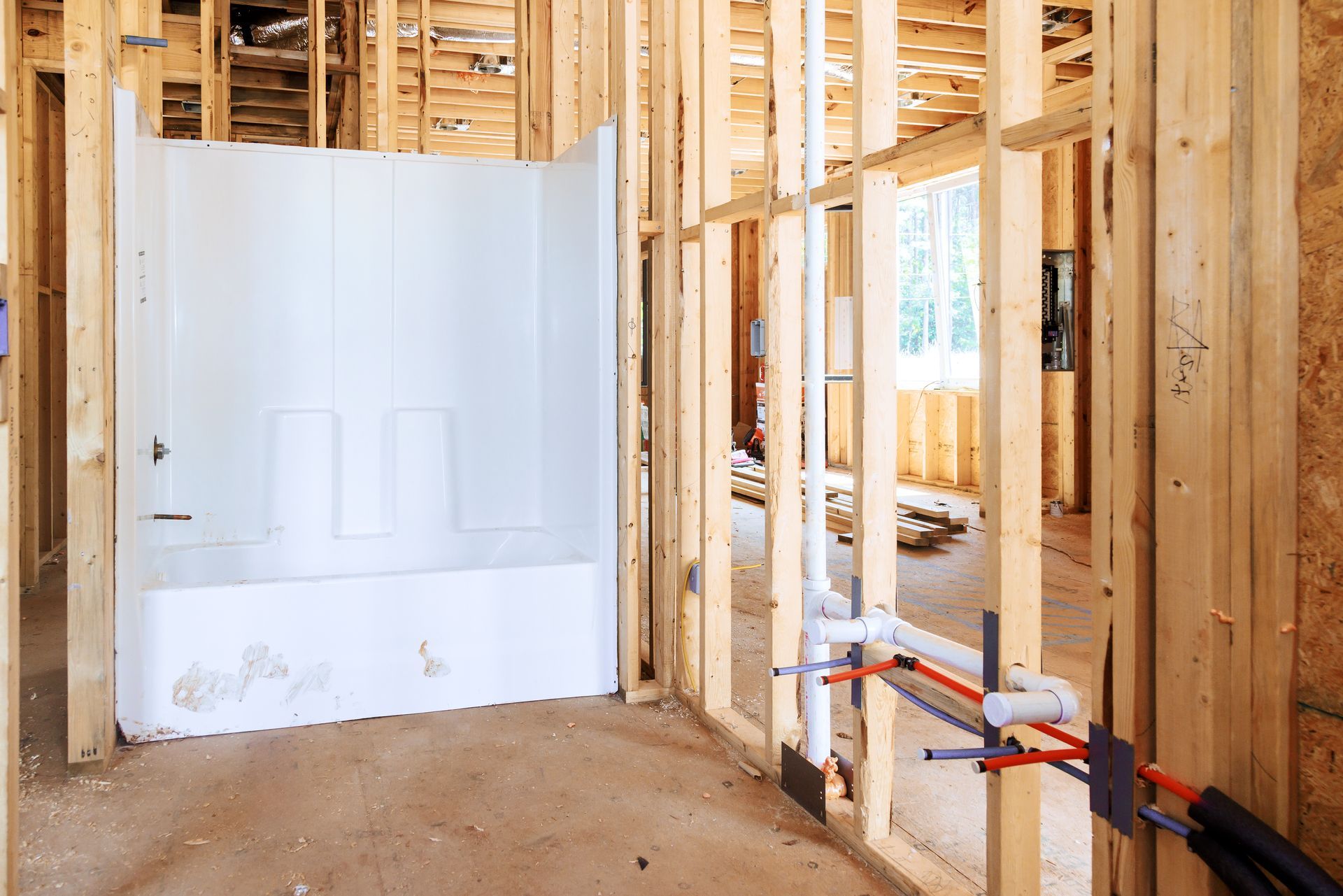 Bathroom under construction with exposed framing and installed white bathtub.