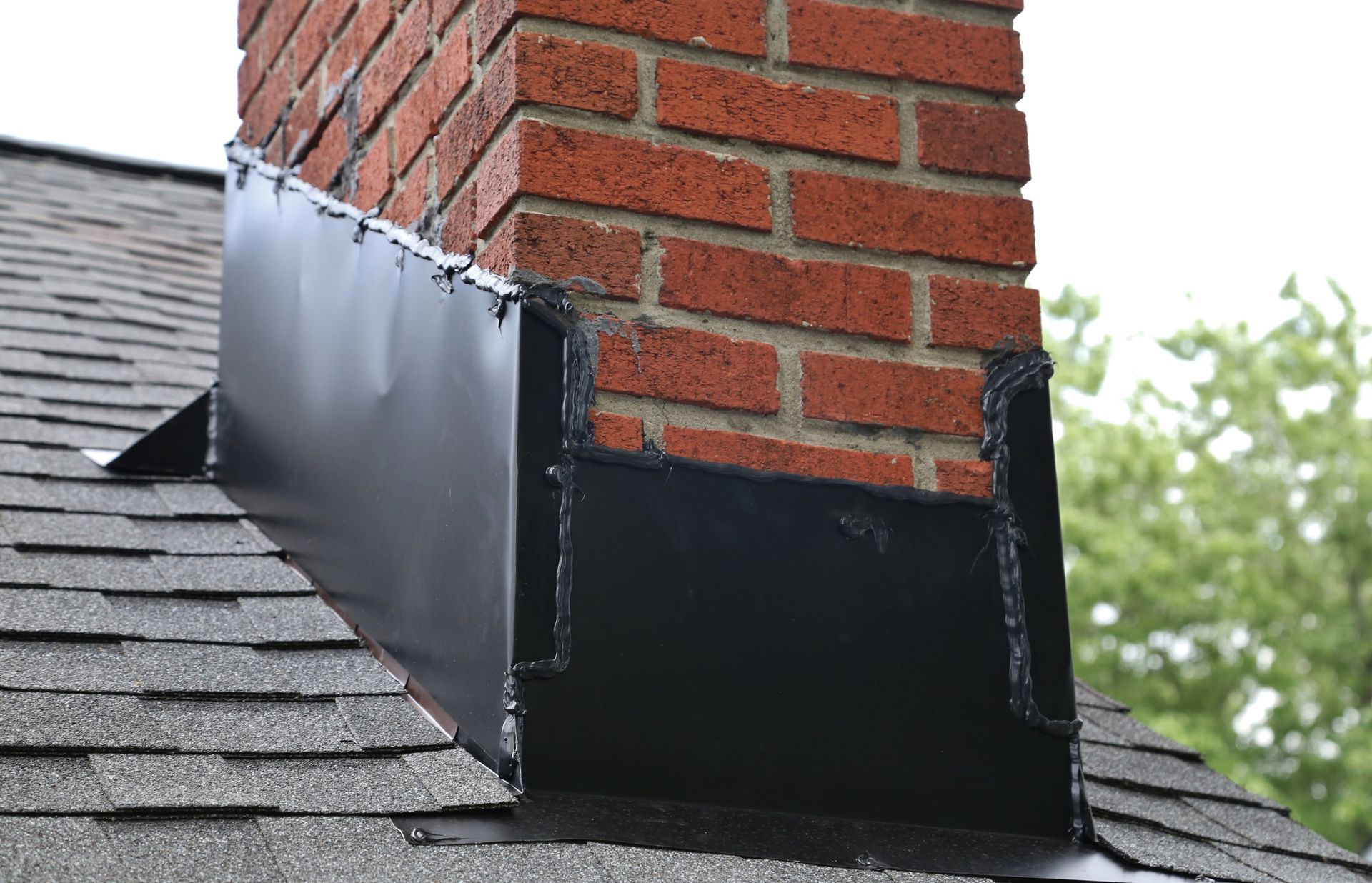A brick chimney on top of a black roof.