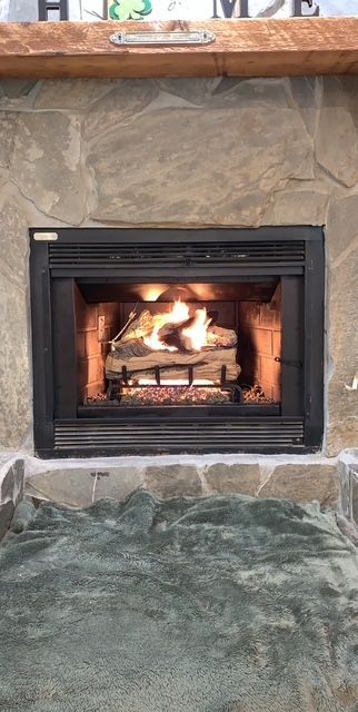 Lit fireplace with orange flames in a black framed hearth beneath a wooden mantel.