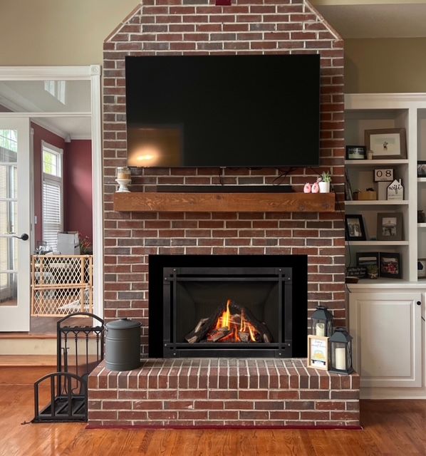 Brick fireplace with mounted TV, lit fire, and built-in shelves in a cozy living room.