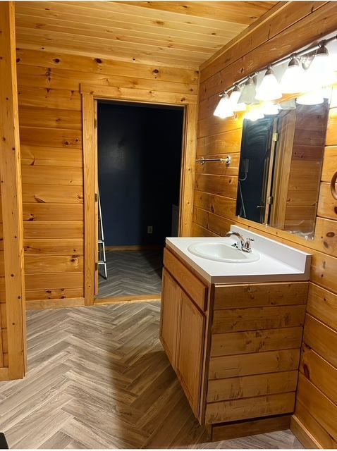 Wood-paneled bathroom with a vanity, lit mirror, and open doorway to a dark hallway