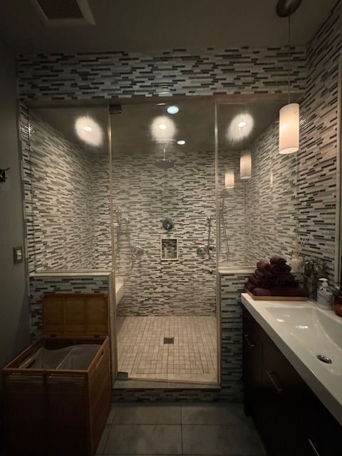 Modern bathroom with tiled glass shower, toilet, and vanity sink with mirror lights.