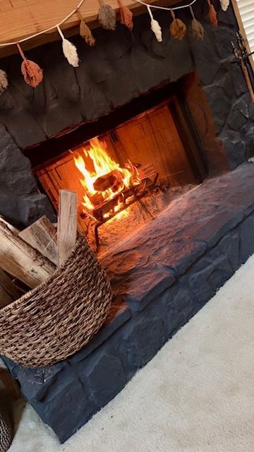 Stone fireplace with a glowing fire, black hearth, and woven basket on a light rug.