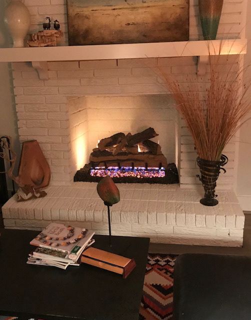 Cozy living room fireplace with glowing fire, white brick mantel, and decorative vases and bookshelves