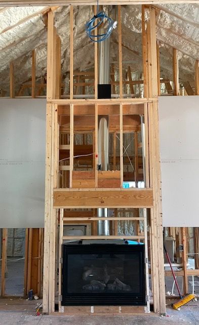 Framed house interior with vaulted ceiling, exposed studs, and a fireplace opening below