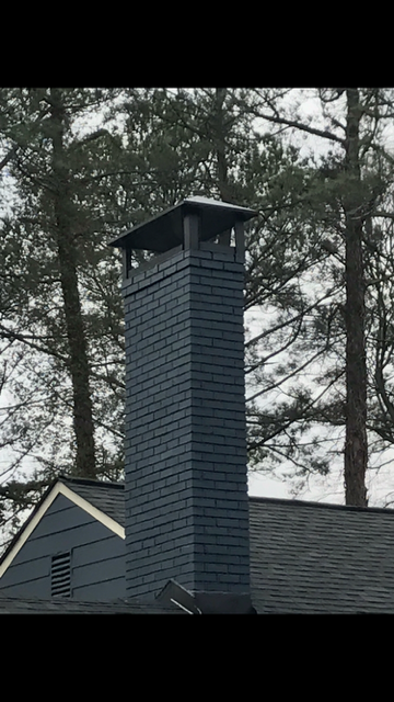 Dark blue chimney on a house roof with trees in the background