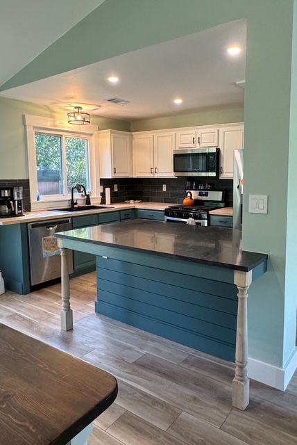 Modern kitchen with blue island, white cabinets, black countertops, and recessed lighting