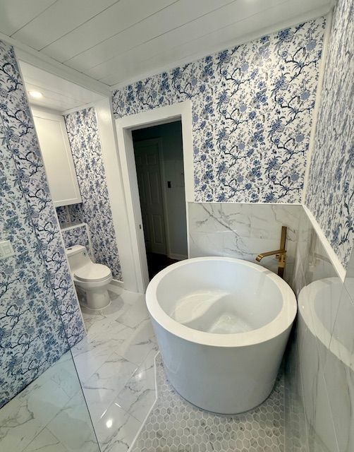 Modern bathroom with blue floral wallpaper, white tub, toilet, and marble tile floor