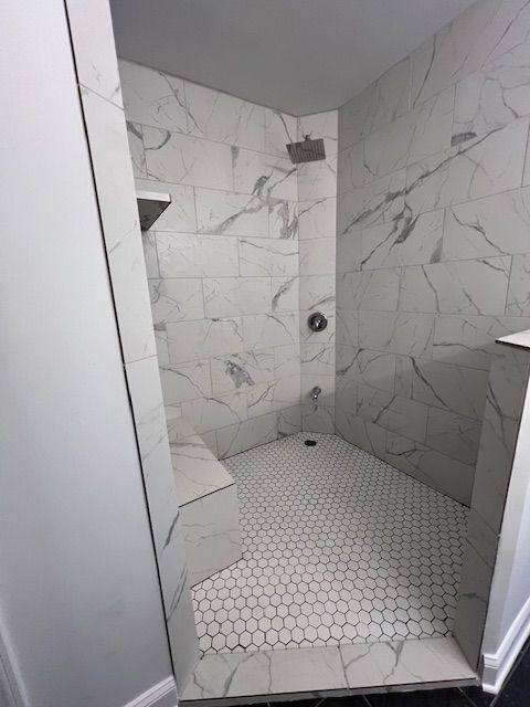Empty marble-tiled shower with hexagon floor and built-in corner bench.