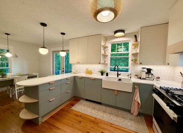 Bright modern kitchen with white cabinets, teal accents, island, pendant lights, and wood floors