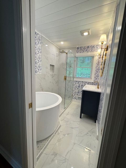 Small bathroom with white tub, marble-look tile, vanity, and window blinds.