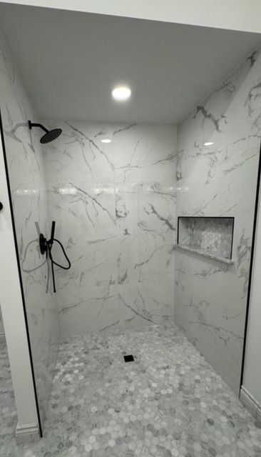 Empty marble-tiled shower with recessed shelf, black shower fixtures, and a ceiling light.