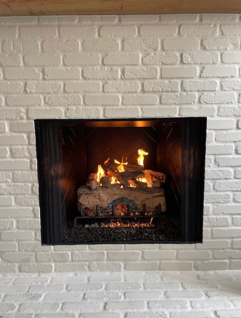 Lit gas fireplace set into a white brick wall.