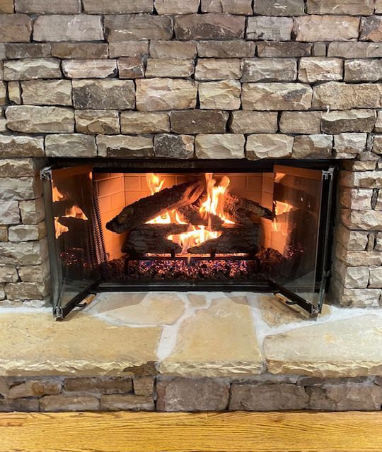 Lit stone fireplace with a burning fire and black glass doors open outward.