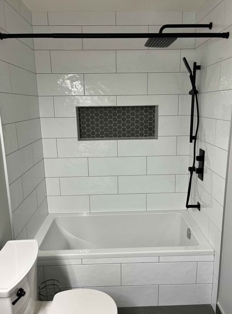 Bathroom with a white tub-shower, tiled walls, black shower fixtures, and a small window.