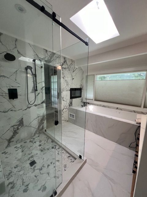 Modern marble bathroom with glass shower, skylight, and a large soaking tub by a window