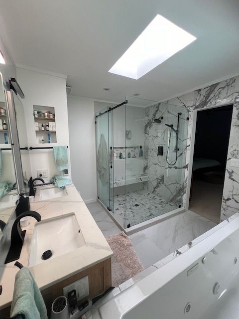Modern bathroom with glass shower, vanity sink, skylight, and marble tile accents
