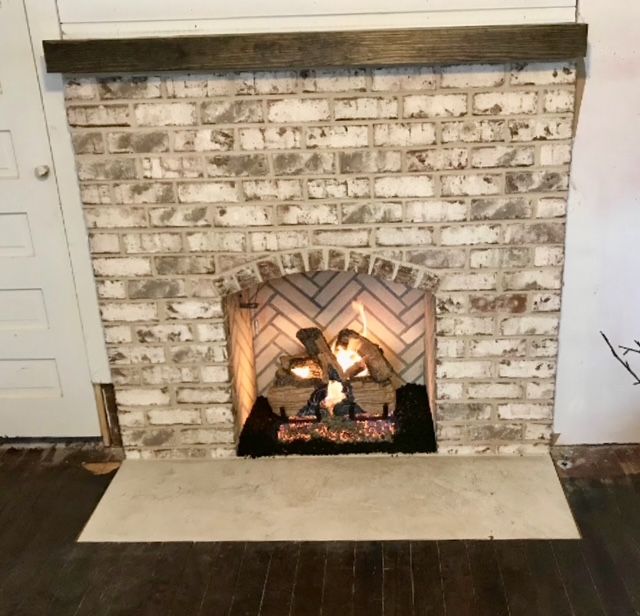Lit brick fireplace with a decorative fire, white mantel, and dark wood floor in a living room