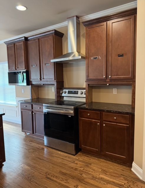 Modern kitchen with dark wood cabinets, black stove, stainless hood, and hardwood floor