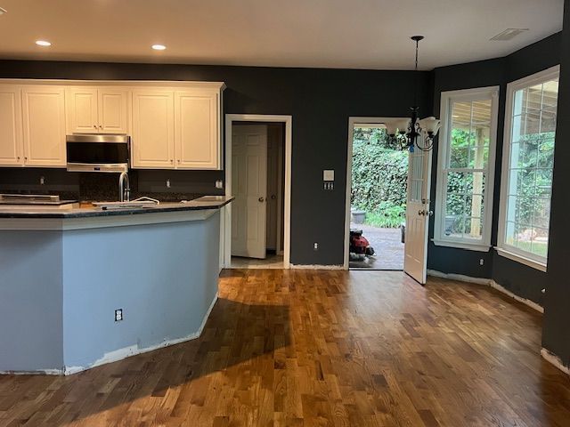 Open kitchen and living room with hardwood floors, light cabinets, blue half wall, and windows by a glass door.