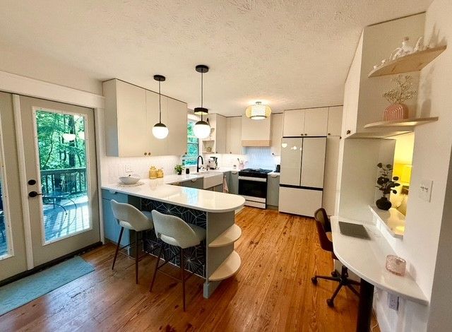Bright open kitchen and dining area with white cabinets, wood floors, and a central island with stools