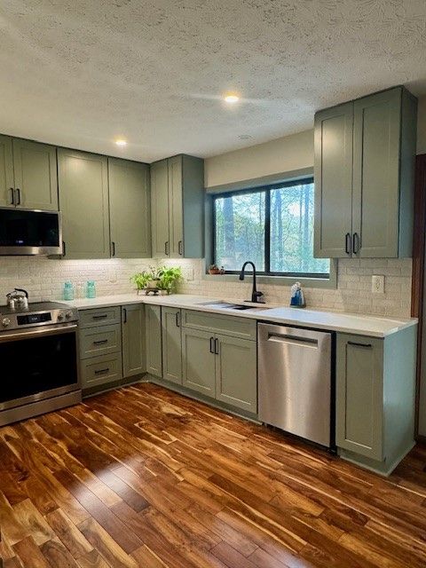 Modern kitchen with sage cabinets, stainless appliances, granite counters, and a window over the sink