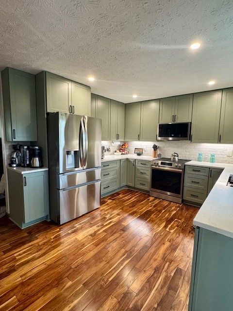 Modern kitchen with sage cabinets, stainless steel appliances, and warm wood floors.